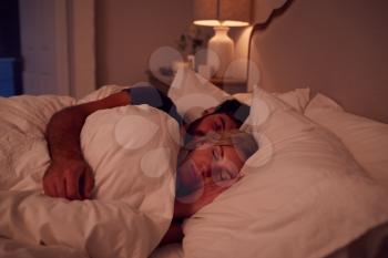 Night Shot Of Peaceful Couple Asleep In Bed Cuddling Together