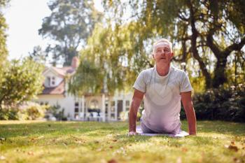 Senior Man At Home In Garden Wearing Fitness Clothing Sitting Doing Yoga Exercise On Mat