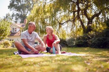 Senior Couple At Home In Garden Wearing Fitness Clothing Relaxing After Outdoor Yoga Class