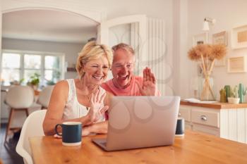 Retired Couple At Home In Kitchen Using Laptop For Video Call With Family