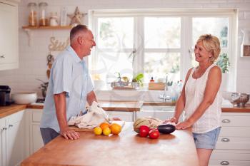 Retired Couple Unpacking Local Food In Zero Waste Packaging From Bag In Kitchen At Home