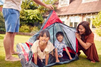 Asian Family In Garden At Home Putting Up Tent For Camping Trip Together