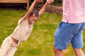 Asian Father Swinging Daughter By Arms As They Play Game In Garden Together