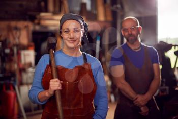 Portrait Of Male And Female Blacksmiths Holding Tools Standing In Forge