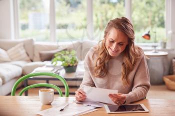 Woman With Digital Tablet Sitting At Table At Home Reviewing Domestic Finances