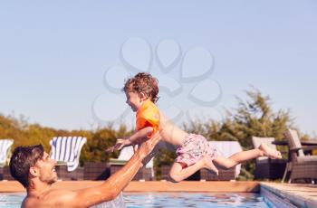 Father And Son In Outdoor Pool On Summer Vacation Teaching Son To Swim With Inflatable Armbands
