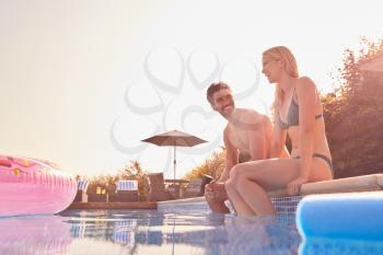 Loving Couple On Summer Vacation Sitting On Edge Of Swimming Pool