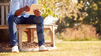 Close Up Of Man Sitting On Bench Under Tree In Summer Park Using Digital Tablet