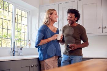 Couple With Pregnant Wife In Kitchen Talking And Drinking Coffee Together