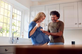 Couple With Pregnant Wife In Kitchen With Husband Touching His Wife's Bump