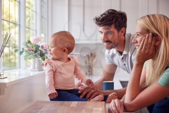 Family With Baby Daughter Having Fun Playing Game Sitting In Kitchen Together