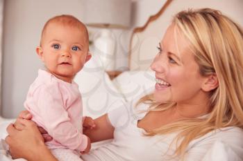 Loving Mother In Bed Playing Game With Baby Daughter Wearing Pyjamas