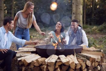 Group Of Friends Camping Sitting By Fire In Fire Bowl Toasting Marshmallows Together