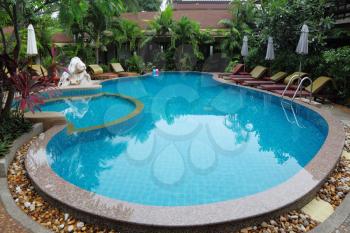 Whimsically curved pool with crystal clear water surrounded by palm trees, statues and sun loungers
