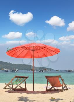 Tropical paradise on the bank of the azure sea. A red beach umbrella and chaise lounges on white sand
