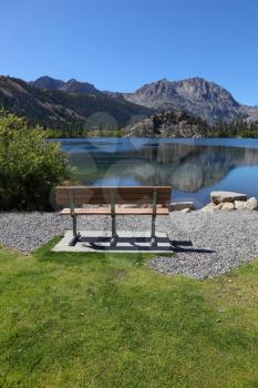 Cosy bench on the shore of Gull Lake. A bright sunny day, the mountain is reflected in the smooth water of the lake