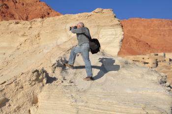 Yellow clay canyon in Dead Sea. An elderly white-haired man with a passion photographs. 