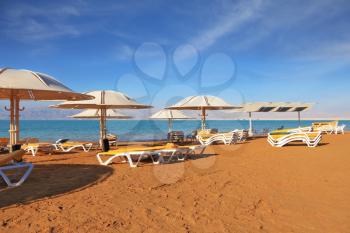 A magnificent beach with clean yellow sand on the shore of the Dead Sea. Guests of the hotel - beach umbrellas and beach loungers