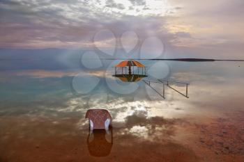 A stunning visual effect on the Dead Sea. Sun rays and picturesque gazebo for bathersare are reflected in a smooth sea surface.