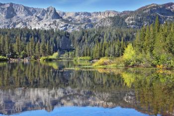 A lovely shallow lake in the mountains of California. In the smooth water surface reflects the majestic mountains and pine forests