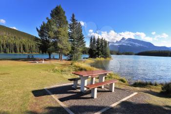 A lovely spot for a picnic by the lake - a wooden table and bench. Quiet shallow lake in Banff National Park in Canada. Sunset