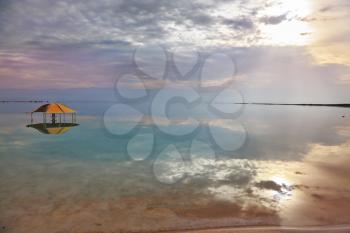 The picturesque red gazebo in the water near the shore. Excellent optical effects and reflections of clouds and sun in the water. Winter in the Dead Sea