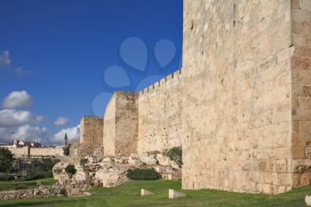 Defensive wall of the ancient holy Jerusalem, lit by the bright sun. Wonderful green lawn