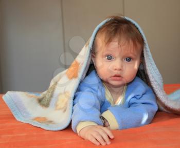 Charming blonde baby with blue eyes covered with a blanket looking at the camera