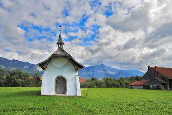 Small rural chapel on a green meadow. Picturesque forged door decorated rows of round rivets. A warm day in Southern France