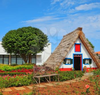 Old house-museum of the first settlers on the island of Madeira. Charming white cottage with a thatched roof and gable small garden with flowers