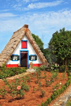 Charming white cottage with a thatched roof and gable small garden with flowers. Picturesque house-museum of the first colonists to Madeira. 