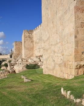 Defensive wall of the ancient holy Jerusalem, lit by the bright sun. Wonderful green lawn