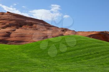 Bright green field for a golf among hills from red sandstone