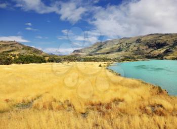 The sharp strong wind bends the yellowed grass. Emerald Lake is covered by waves.  National Park Torres del Paine in southern Chile, in Patagonia