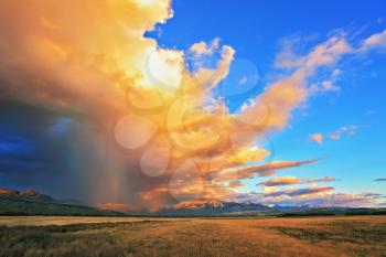 Summer rain. The beautiful huge cumulonimbus cloud is shined with the sunset. Rain streams are shone with orange light. The cloud hangs over the gravel road