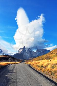 National Park Torres del Paine in southern Chile. A dirt road leads to the distant mountains. A huge cloud in the form of a burning candle flies away.