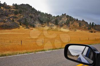 The automobile mirror reflects road and an autumn landscape of the American West