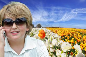 Beautiful blond boy talking on a cell phone against a bright flower of the field