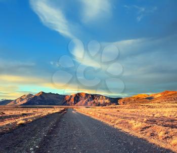 Argentine Patagonia.  The gravel road between the endless pampas. The setting sun illuminates the mountains and steppe red