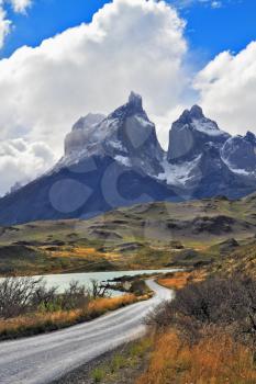 Grandiose landscape in the Chilean Andes. The road between turned yellow hills goes to snow-covered black rocks. Patagonia