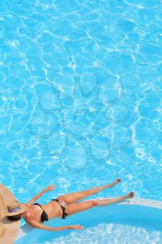 Slender young girl resting and sunning in the clean and clear pool water
