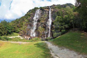 Double falls in mountains of northern Italy. Parallel streams of water on a green overgrown hillside. The photo is made by a lens Fisheye