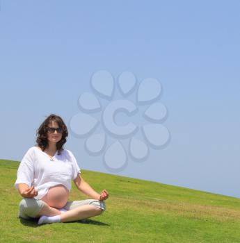 Happy young pregnant woman doing yoga on the lawn by the sea.