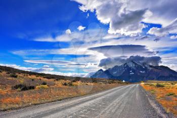 Incredible clouds over the mountain glaciers. Stunning sunset in the Chilean Patagonia. The dirt road leads to the mountain range