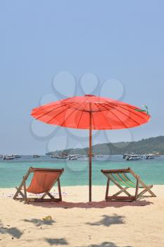  A red beach umbrella and chaise lounges on white sand. Tropical paradise on the bank of the azure sea

