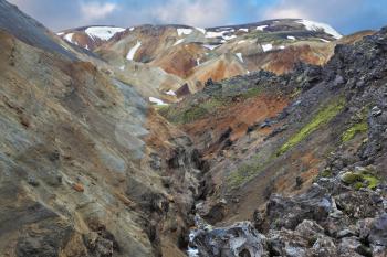 Pieces of gray and black lava, sometimes covered with green moss. In the background -  orange and blue rhyolite mountains. National Park Landmannalaugar in Iceland