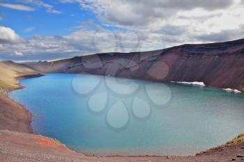 Oval blue lake in the crater of the volcano cooled down. Steep banks of the lake of red rhyolite. Iceland in July