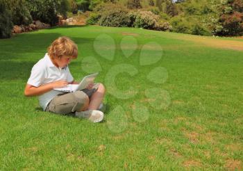  The beautiful boy with gold hair  played on laptop on a lawn in a city park