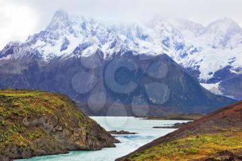 Neverland Patagonia. Snow-capped mountains of the national park Torres del Paine. Icy emerald water of the mountain river flows between hills