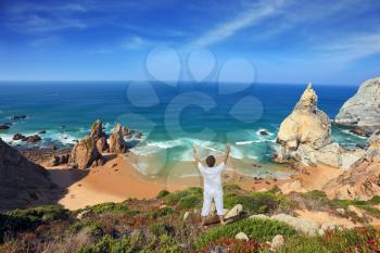 Small beautiful beach on the Atlantic coast. Middle-aged woman dressed in white doing yoga. The seaside resort of Sintra